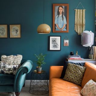 Living room detail with teal walls, cream carpet, vintage blue green velvet sofa and orange leather sofa, 1970s ombre glass pendant