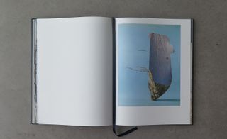 Image of an open book, Titled Marseille Je T’aime- One page blank, the other showing a large rock on a blue background