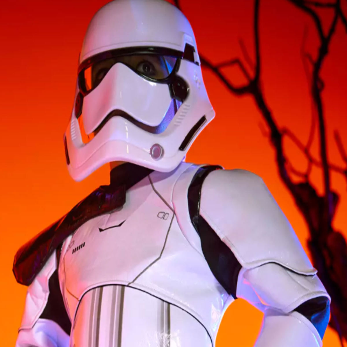 A white robotic costume featuring black eyes and mouth is worn by someone in front of an orange background.