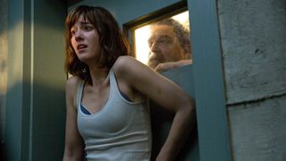 Michelle looks scared as Howard peers at her through a small window in 10 Cloverfield Lane