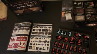Resident Evil: The Board Game box, game rulebook, and miniatures on a black table