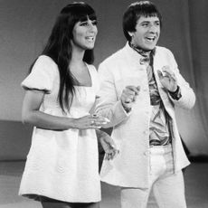 A black and white photo of Sonny and Cher from 1965 singing in white outfits