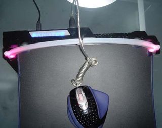The Headshot Controller's coiled cord sits above the mouse pad on the cable arch.
