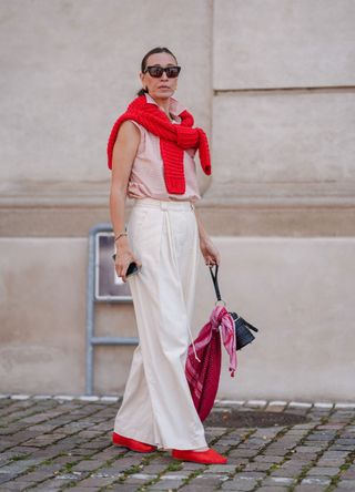 Alana Hadid wearing bright red ballet flats with wide leg trousers and a matching red jumper tied around her shoulders