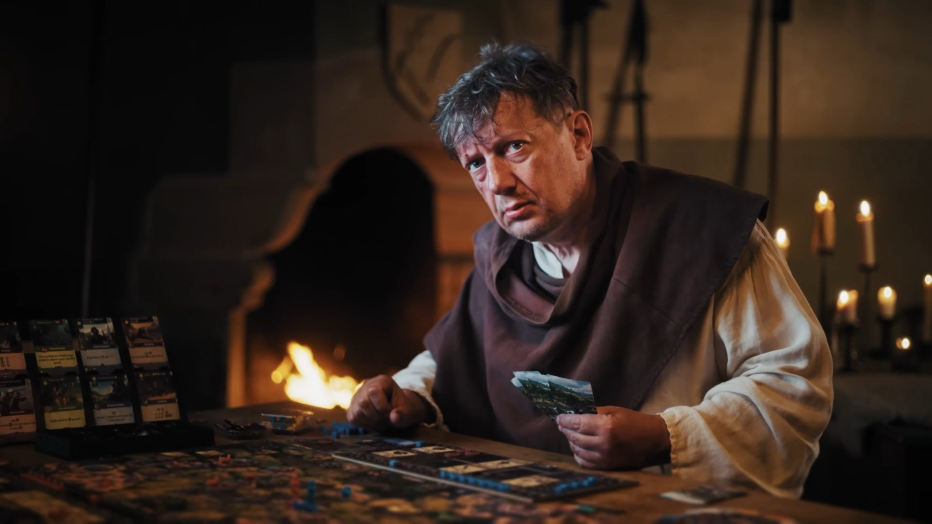 A man in peasant clothing plays the Kingdom Come: Deliverance board game.