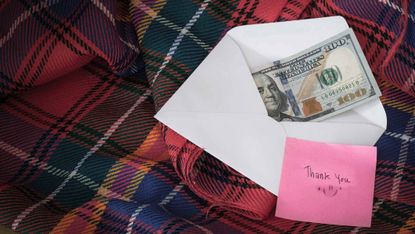 Money in a white envelope, put on a blanket, along with a thank you message. - stock photo