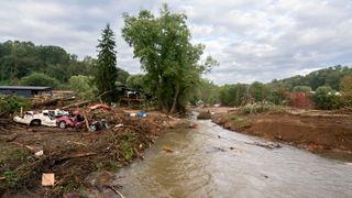 smashed cars and other debris lay strewn across a muddy field beside a brown river