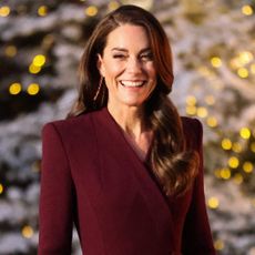 Kate Middleton in a burgundy coat in front of trees decorated for Christmas