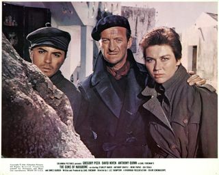 two men and a woman dressed in trench coats look mysterious in a still of the movie The Guns of Navarone