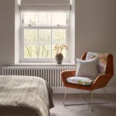 Carpeted bedroom with an orange accent chair sitting in front of the window