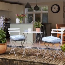A patio with a white bistro set with striped seat cushions and potted plants on the table and around the set
