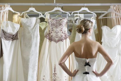 Woman in a wedding dress with her back to the camera, she is looking at a selection of wedding dresses on hangers