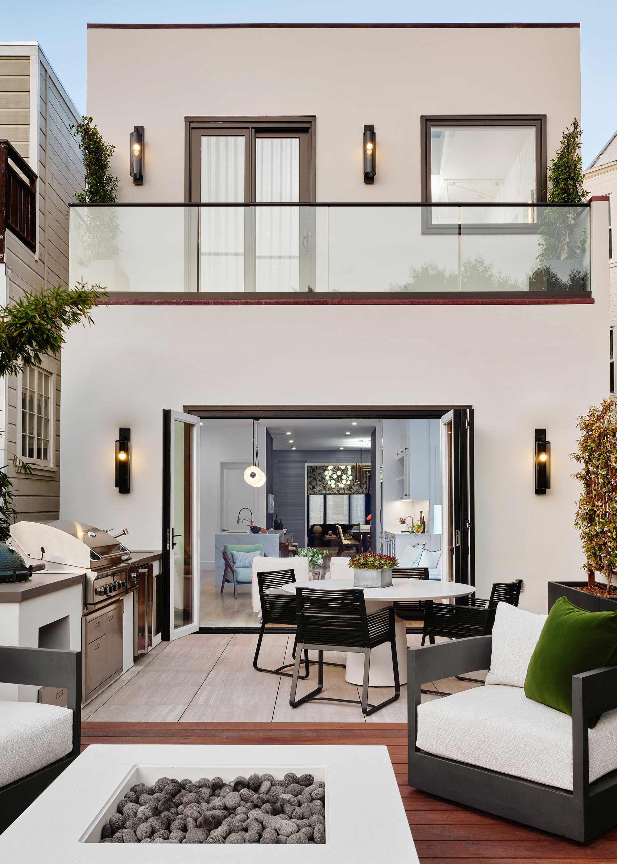 modern white rendered house with first floor balcony and bifold doors leading to outdoor kitchen