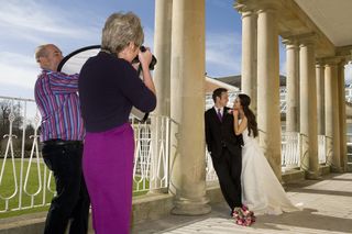 Photographer and assistant taking wedding photos of a bride and groom outdoors, standing in front of Georgian pillars