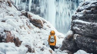 Woman with orange jacket standing below amazing frozen Pericnik waterfall
