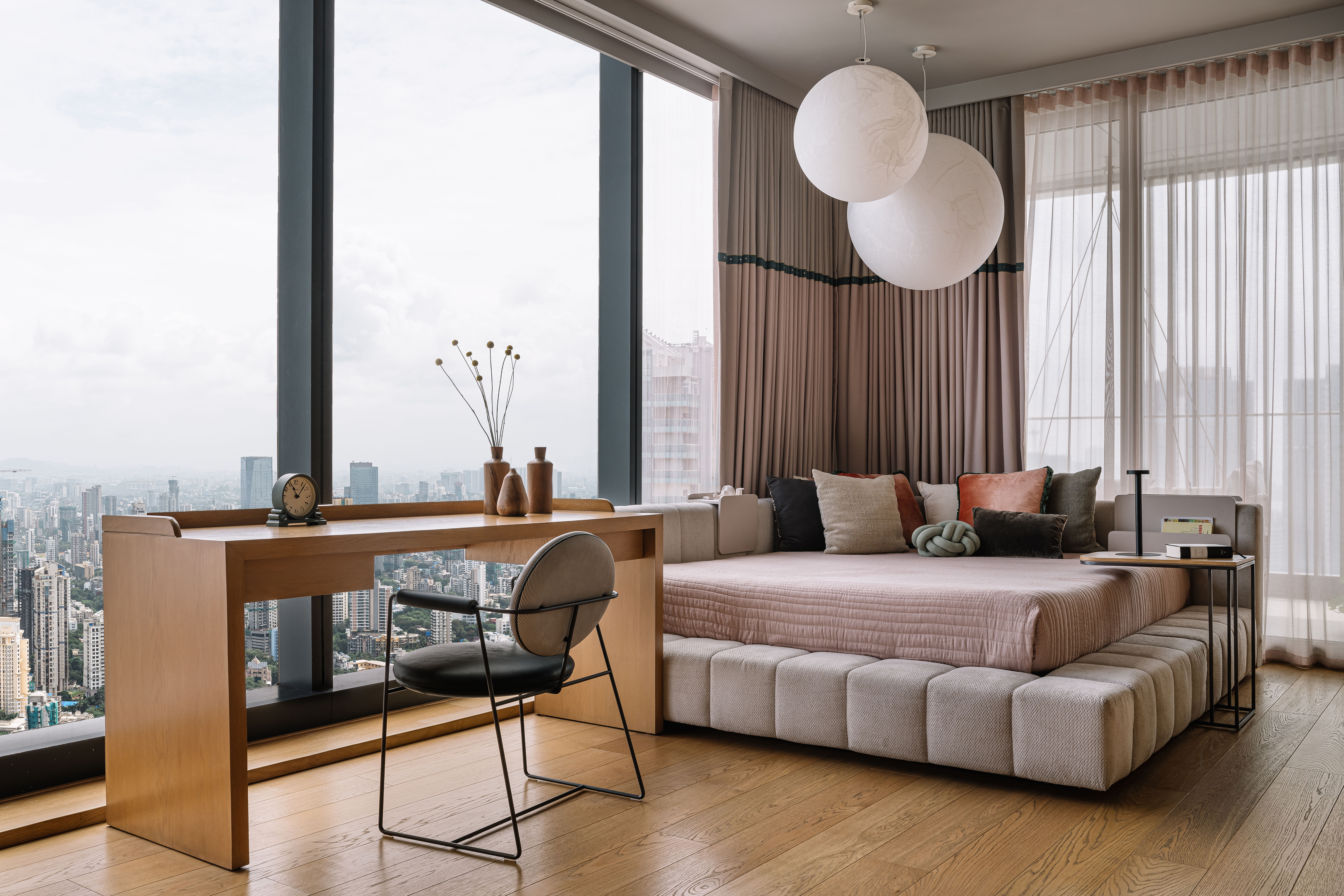 A bedroom with a corner bed, with large lights above it, and a study desk adjacent