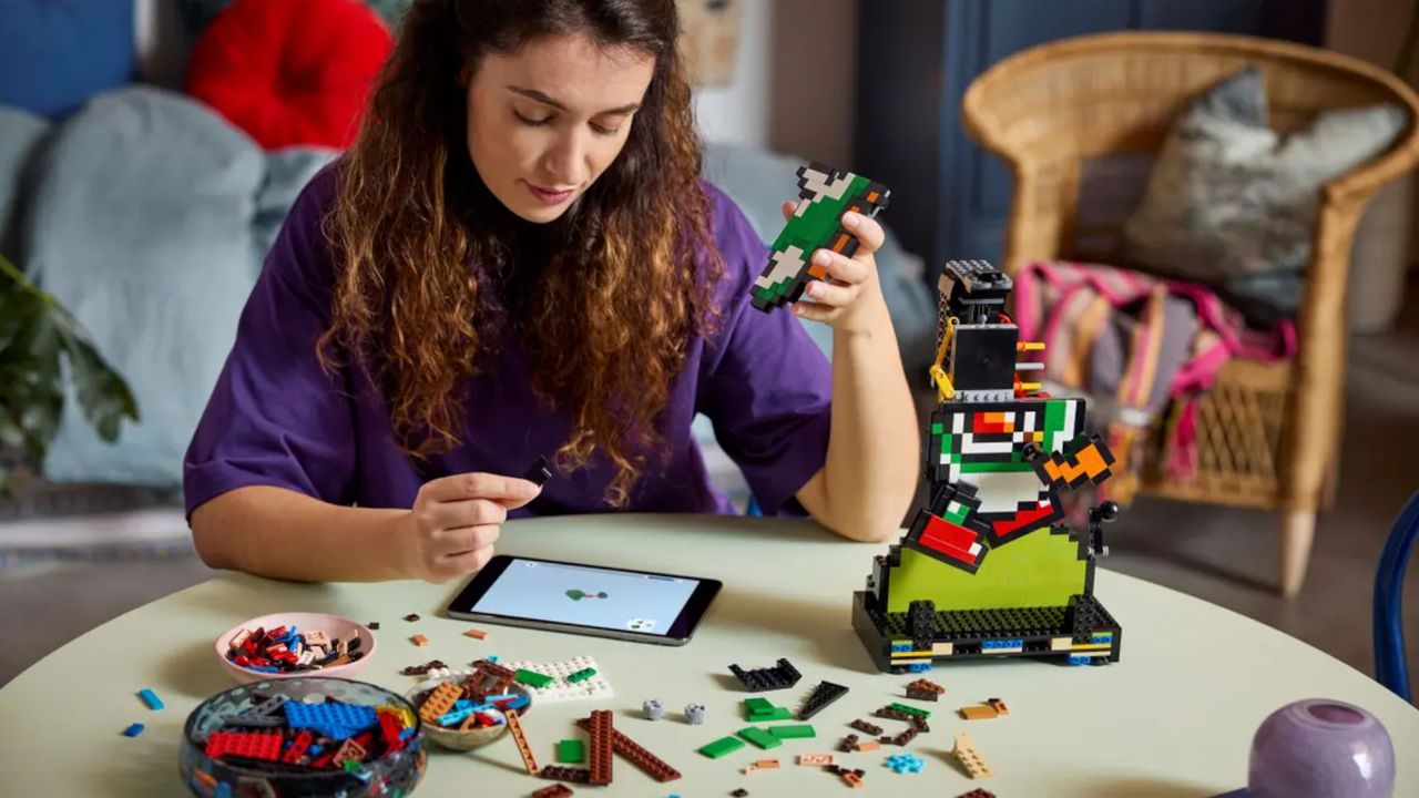 Lego Super Mario World set in construction on a table, with a woman using the instructions to build it