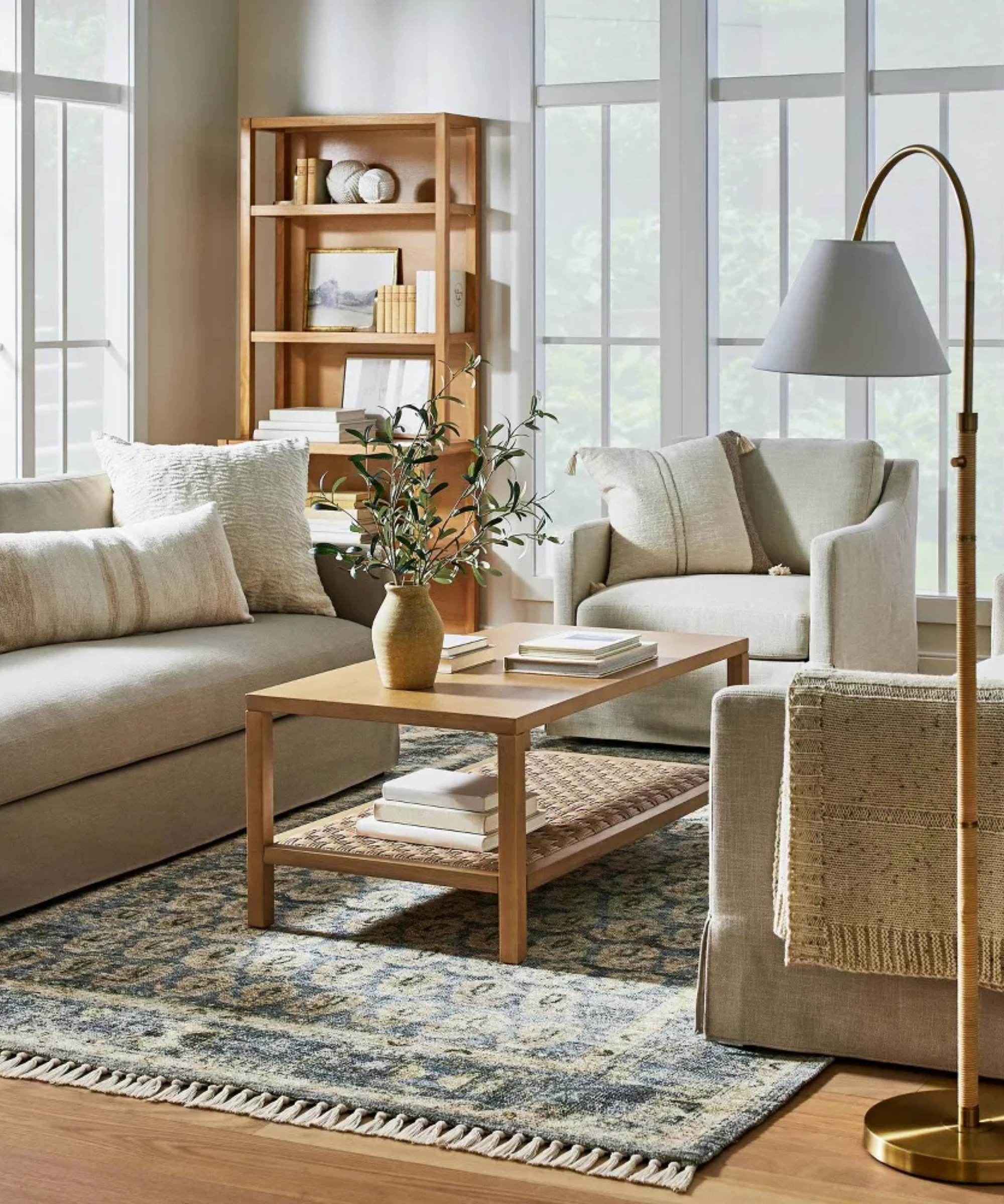 a living room with a beige couch, a beige accent chair, a wood rectangular coffee table with a flower vase on top, and a blue Persian-inspired rug on the floor