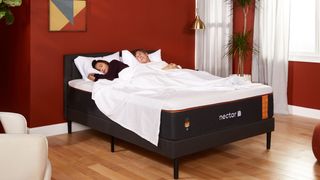 The Nectar Premier Copper Mattress shown at an angle and placed on a black bedframe in front of a deep red bedroom wall