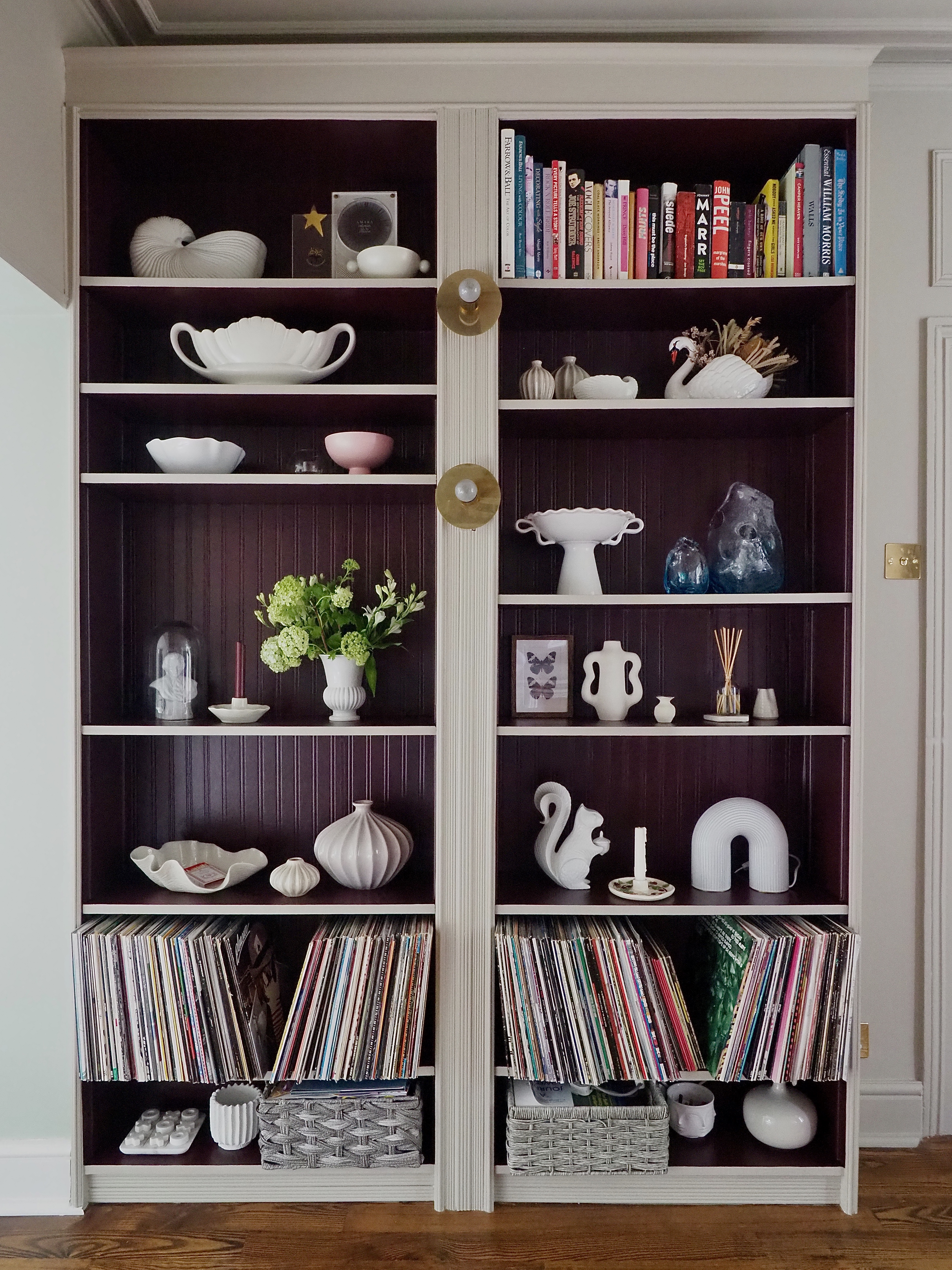 An IKEA billy bookcase with the back of the shelves painted purple. The shelves are decorated with books, decor, and a row of records along the bottom