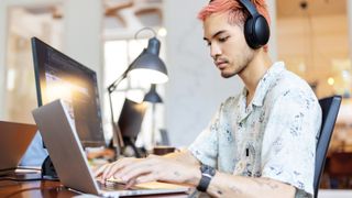 Young person wearing headphones working at a laptop on a desk