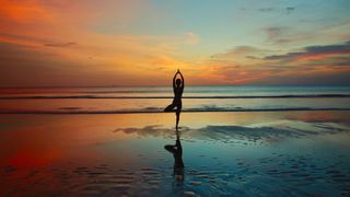 When did yoga originate? Image of person practicing yoga on a beach at sunset