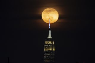 full golden hued moon behind the top of the empire state building.