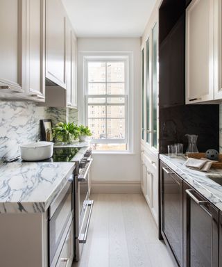 A kitchen with marble counters and backsplash, and dark brown accents