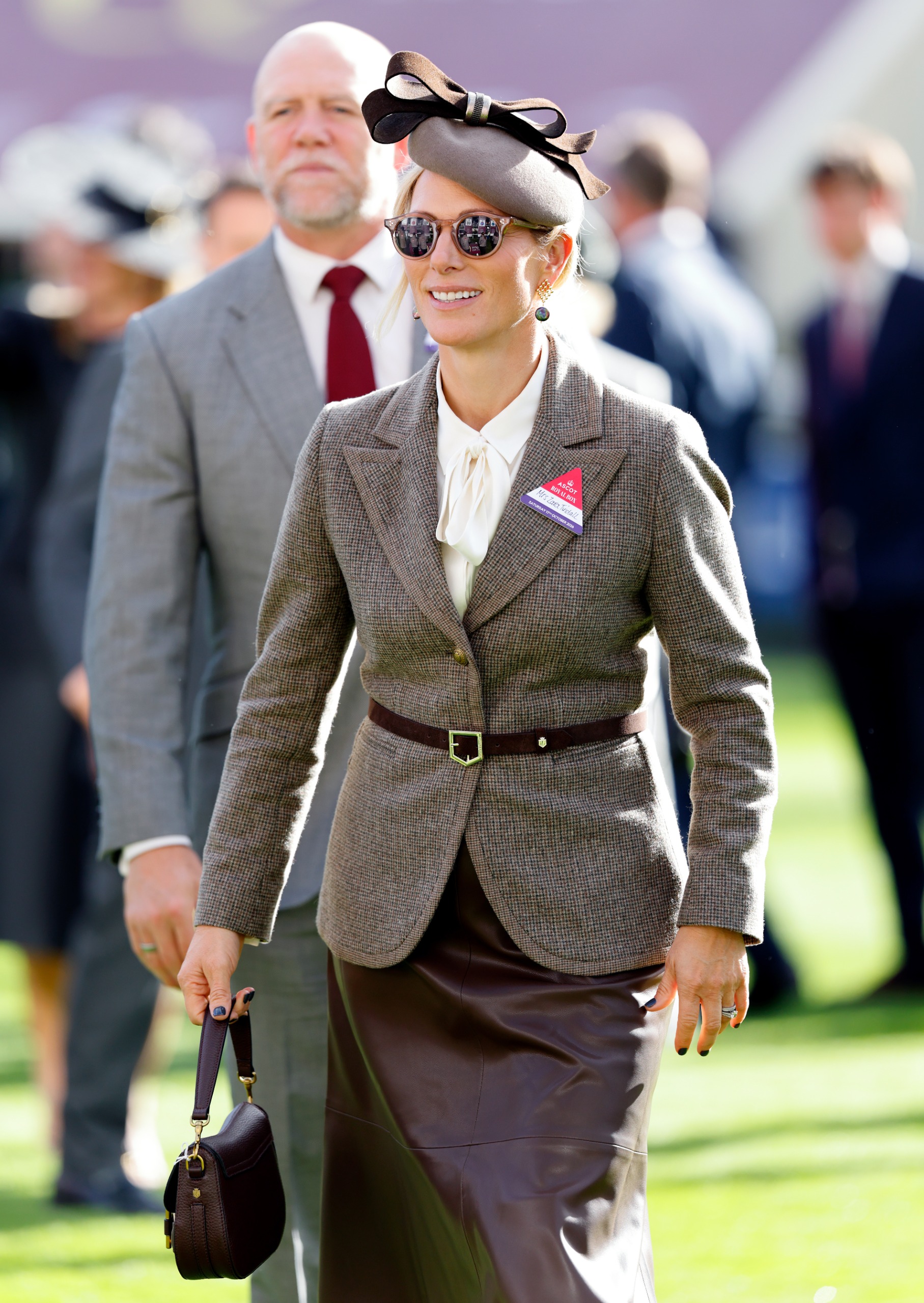 Zara Tindall wearing a brown leather skirt and blazer walking with mike Tindall behind her