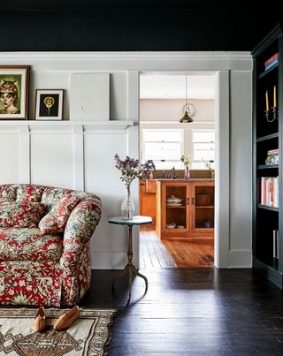 library with red patterned sofa, patterned rug and dark green bookcase