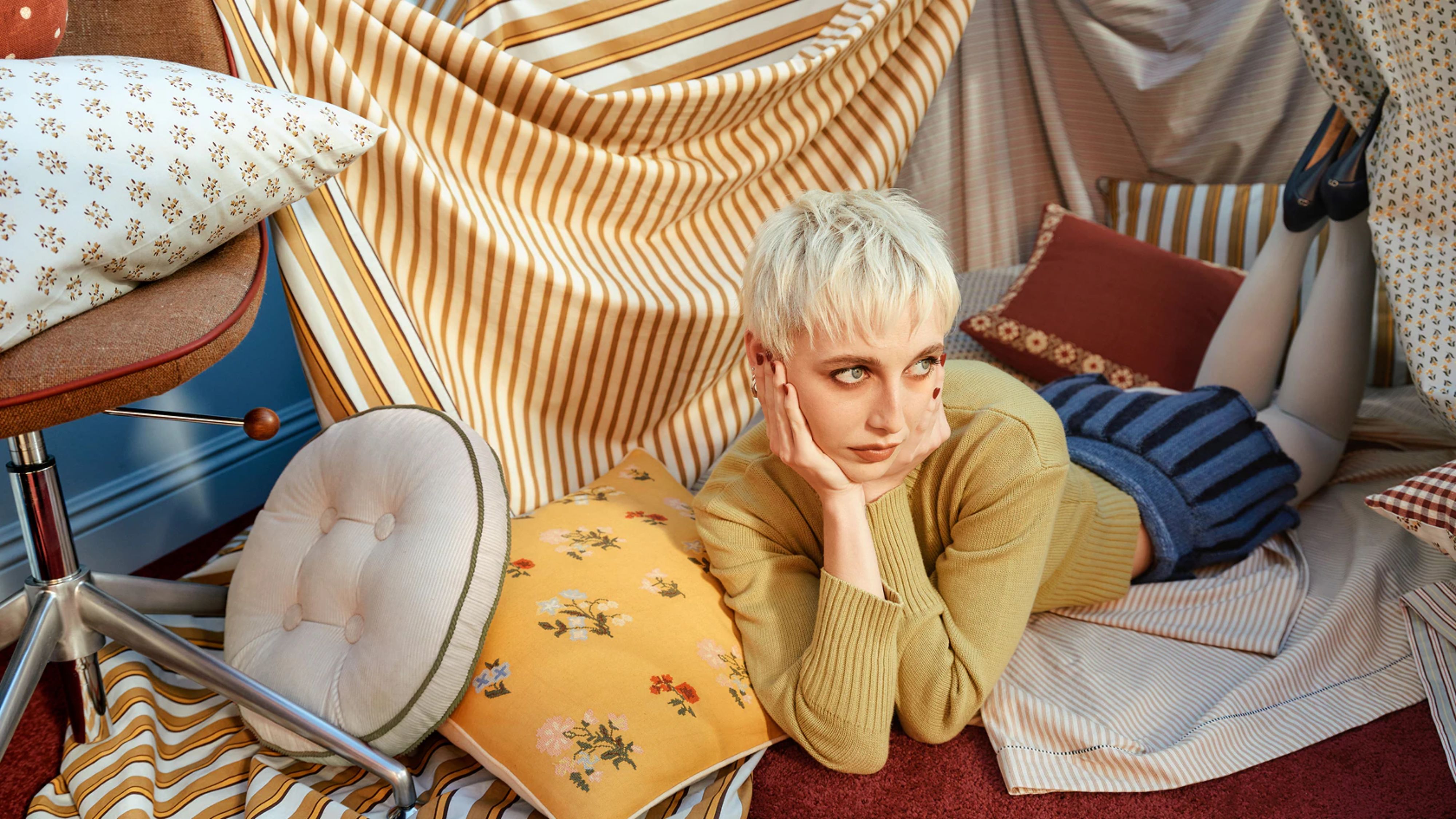 Fashion icon Emma Chamberlain poses on the floor among vintage-inspired cushions and bed linens from her new West Elm home collection. 