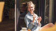 Woman eating breakfast and drinking coffee in the sunshine, representing foods to lower cortisol levels