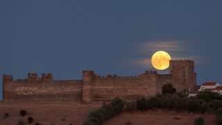 The harvest moon of 2022 rises above an ancient castle in Portugal.