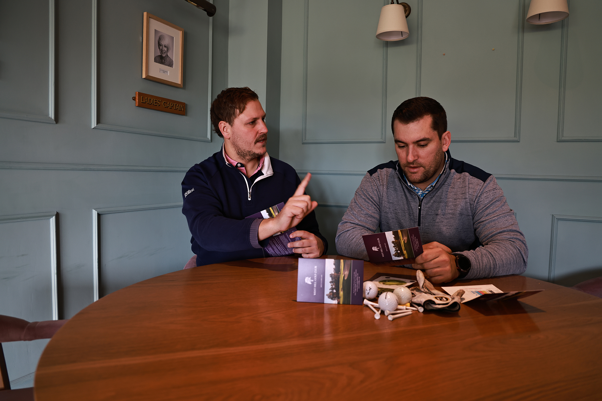 Two male golfers discussing their scorecard after the round, with one looking agitated at the points total of the other golfer in a Stableford competition