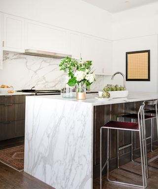 A kitchen with a marble waterfall island and red barstools