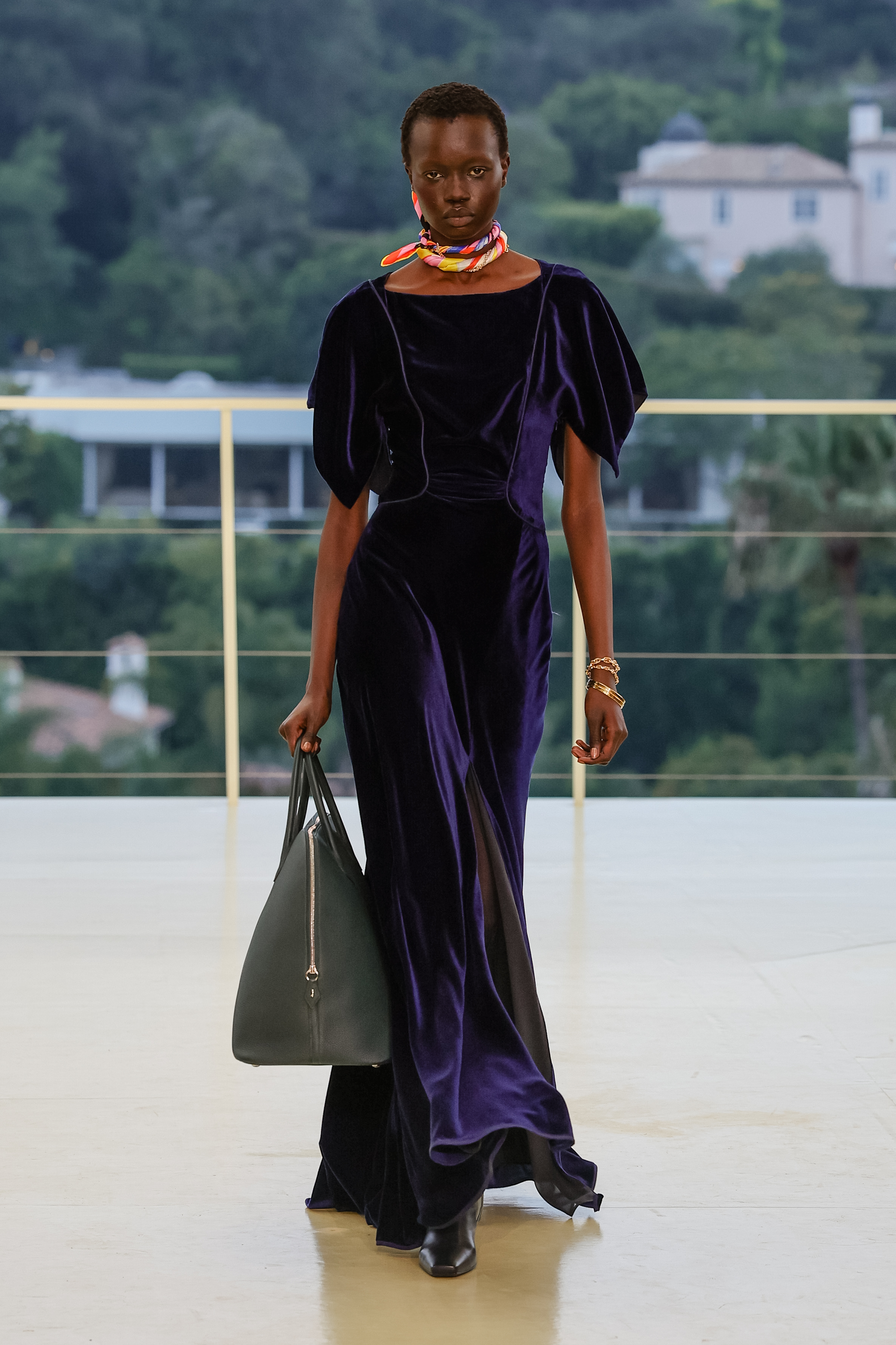 a woman wears a purple dress with a large bag.