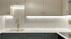 A two-tone kitchen with sage green cabinets at the bottom and cream at the top. The kitchen has a gold tap, gold sockets and brass gold handles
