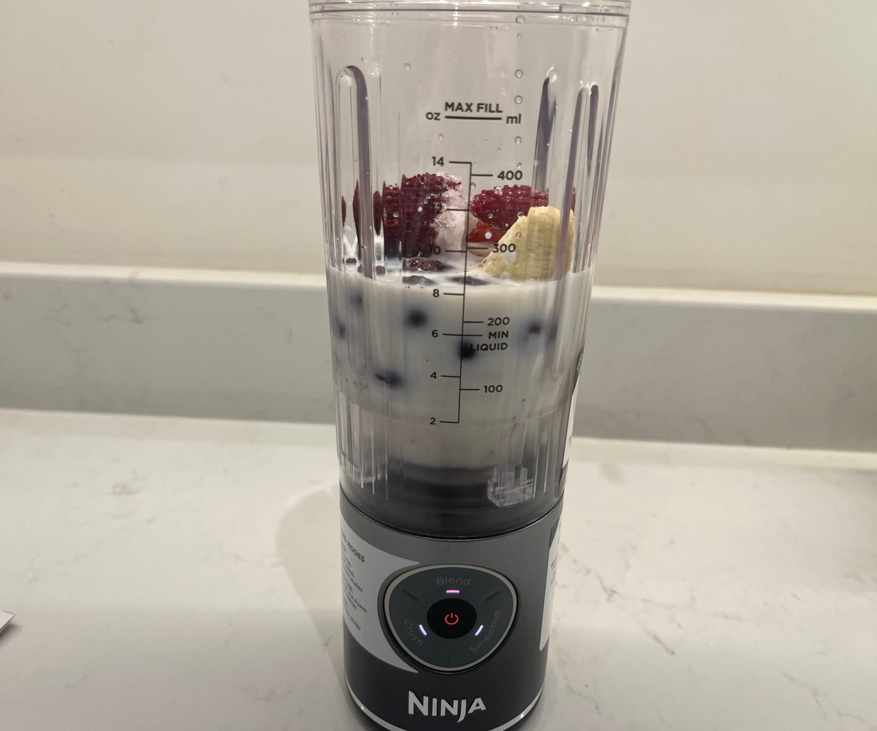 The pitcher of the Ninja Blast Max is filled with milk and fresh berries.