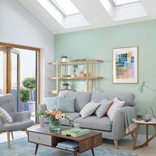 green and white living room with a grey sofa and patterned cushions, with a wooden coffee table decorated with flowers on top of a blue patterned rug