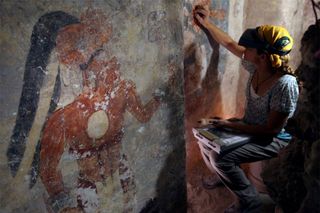 Conservator Angelyn Bass cleans and stabilizes the surface of a wall of a Maya house that dates to the ninth century. The figure of a man who may have been the town scribe appears on the wall to her left.
