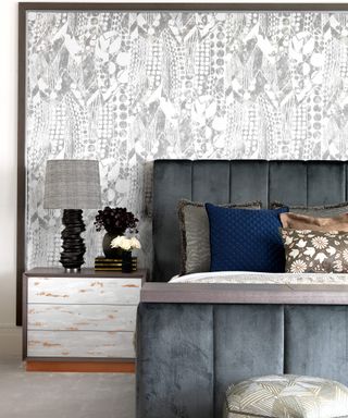 A gray velvet bed with a white and gray patterned wall mural behind