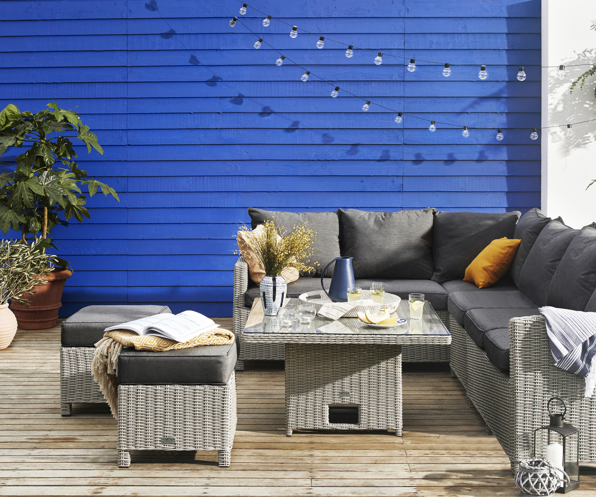 blue painted horizontal fence next to white wall with grey wicker outdoor furniture in front