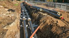 A photo of district heating pipes carrying heat to communities, half-laid in a trench in the ground with construction fencing around it.