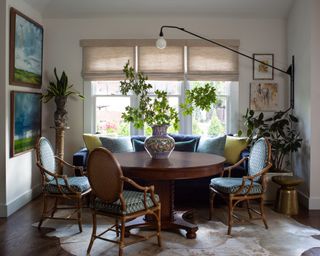 dining room with white walls, blue and green cushions and artwork, wooden round table and blue and wood chairs