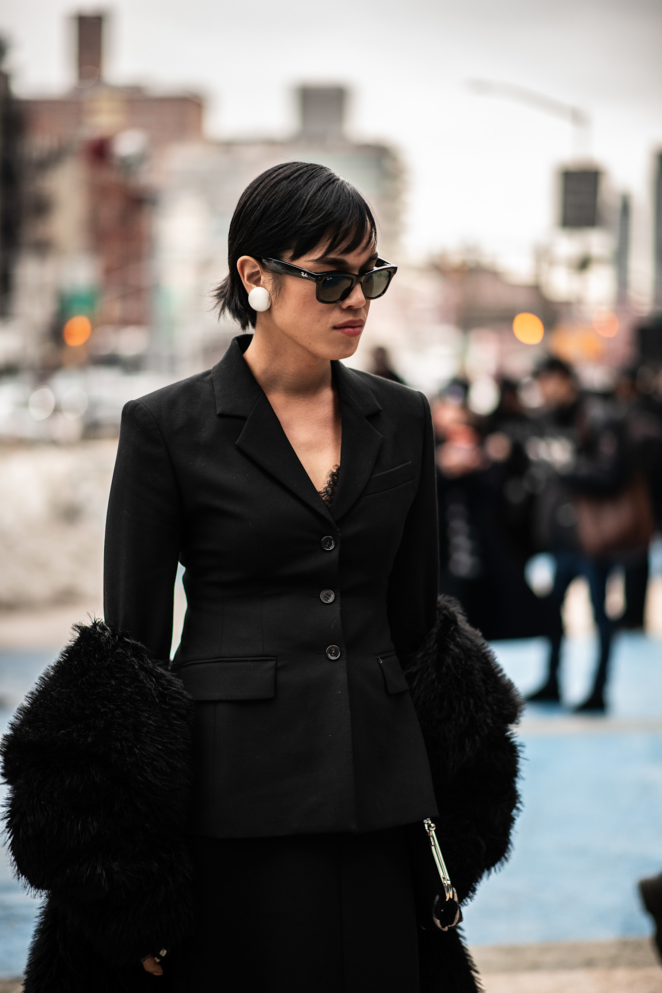 a woman with a short black bob in a black jacket with sunglasses and large pearl earrings