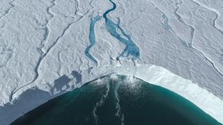 Aerial image of a melting ice shelf next to body of water.