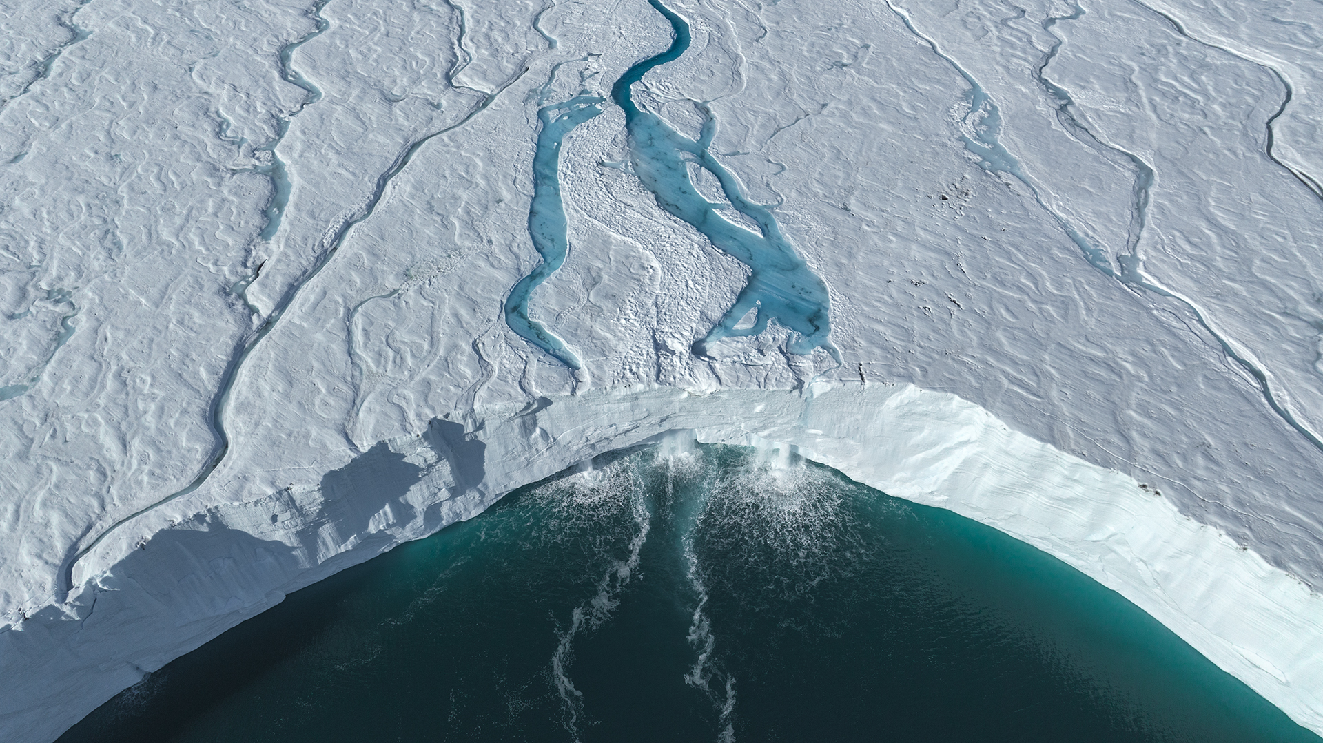 Aerial image of a melting ice shelf next to body of water.