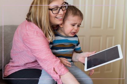 Boy crying holding tablet sat with mum on sofa