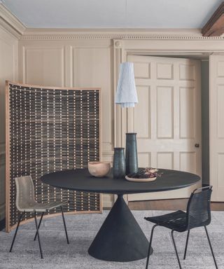 Dining room with a curved room screen, rug and modern furniture, dark grey table and chairs, a pale wooden bowl and vases.