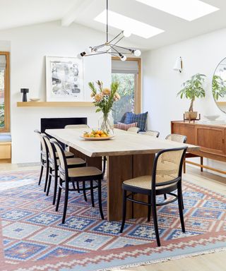A dining room idea with white walls, Scandi-style dining table and chairs, blue and red rug and black sputnik chandelier